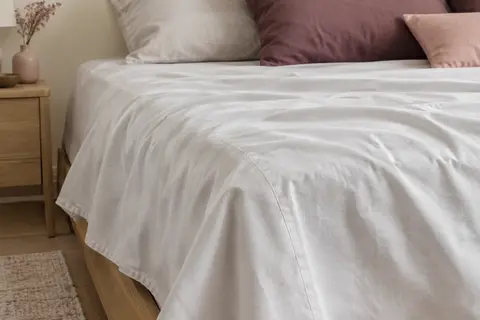 Drap plat uni en coton blanc cassé, posé sur un lit dans une chambre aux tons ivoire et prune doux.