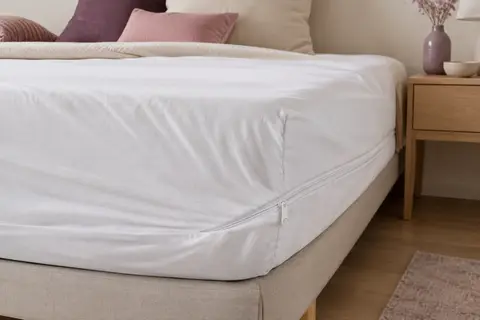 Housse intégrale blanche à fermeture zippée posée sur un matelas dans une chambre aux tons doux.