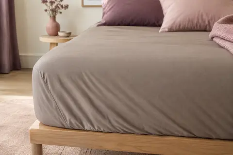 Drap-housse taupe uni posé sur un matelas, avec un tombé souple et des bords ajustés.
