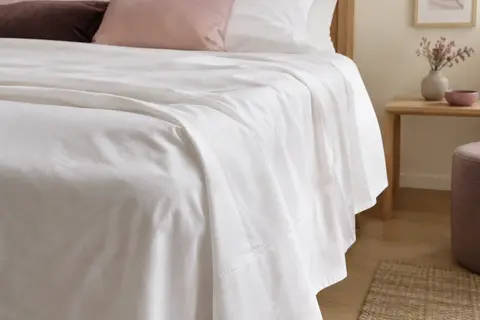 Drap plat blanc en coton posé sur un lit, avec un gros plan sur le tombé et la finition surpiquée.