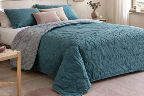 Couvre-lit réversible matelassé turquoise et acier posé sur un lit dans une chambre aux tons doux