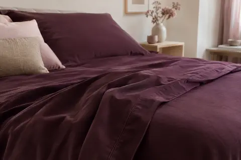 Drap plat uni en coton à la teinte myrtille, posé sur un lit dans une chambre aux tons doux.