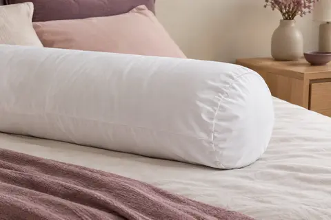 Protège-traversin blanc en molleton de coton posé sur un traversin dans une chambre aux tons doux
