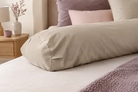 Taie de traversin unie en percale de coton sable, posée sur un lit dans une chambre lumineuse.