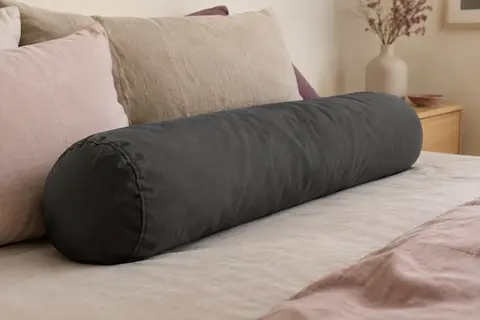 Taie de traversin en coton anthracite uni, posée sur un lit aux tons doux et naturels