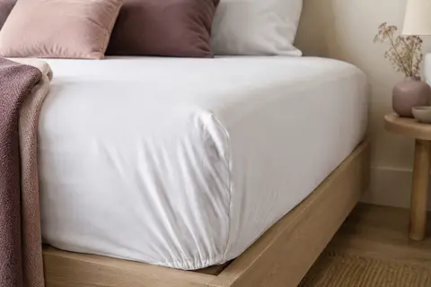 Drap-housse blanc en jersey de coton ajusté sur un lit simple, dans une chambre aux tons doux.