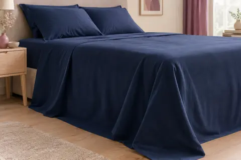 Drap plat bleu foncé en microfibre brossée, posé sur un lit avec une retombée souple sur les côtés.