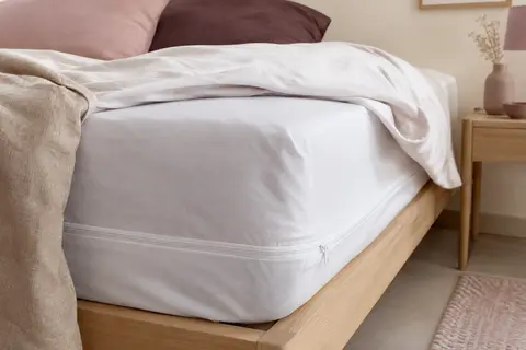 Housse intégrale blanche en coton autour d’un matelas, avec sa fermeture éclair visible dans une chambre douce