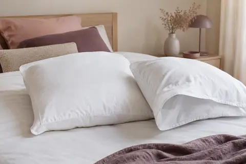 Deux taies d’oreiller blanches en coton, dont une entrouverte pour montrer sa fermeture enveloppe.