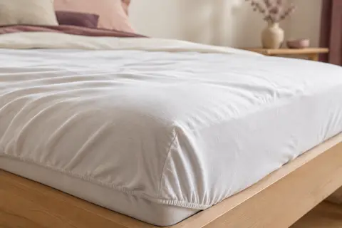 Drap-housse blanc en jersey de coton ajusté sur un matelas, avec un gros plan sur le tissu souple et le bord élastiqué.