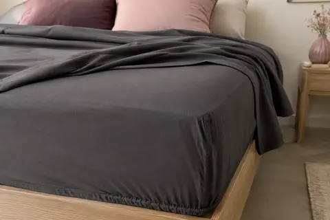 Drap-housse Flowen en microfibre gris foncé ajusté sur un matelas, avec un coin élastiqué visible.