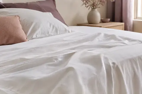 Drap plat blanc en coton tissé posé sur un lit dans une chambre aux tons ivoire et prune doux
