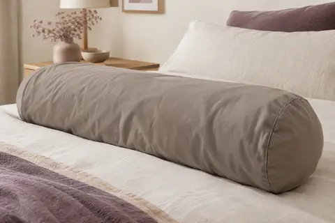 Taie de traversin unie en coton taupe posée sur un lit dans une chambre aux tons doux