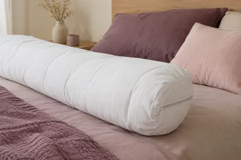 Protège-traversin blanc matelassé en polycoton posé sur un lit aux tons prune doux et sable