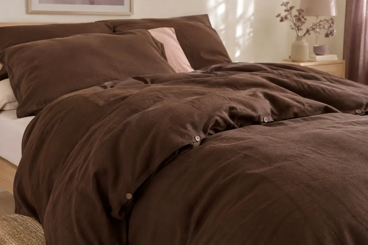 Housse de couette unie en coton lavé chocolat, aux plis souples, posée sur un lit dans une chambre lumineuse.