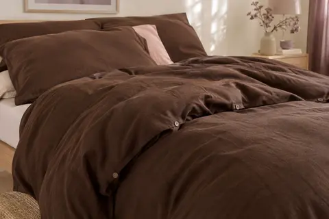 Housse de couette unie en coton lavé chocolat, aux plis souples, posée sur un lit dans une chambre lumineuse.