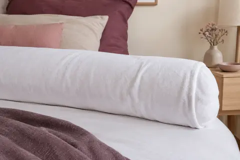 Protège-traversin blanc en molleton installé sur un traversin, avec sa surface textile visible dans une chambre calme.