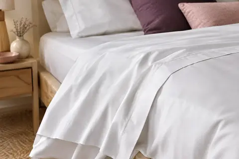 Drap plat blanc en coton satin posé sur un lit dans une chambre aux tons ivoire et prune doux.