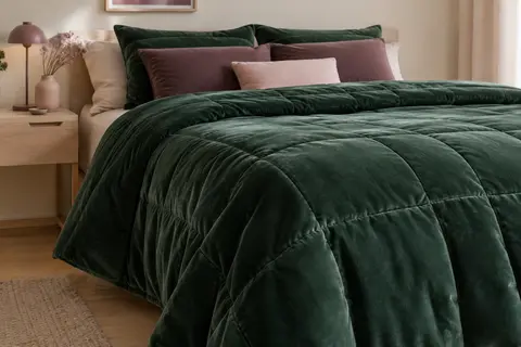 Dessus de lit matelassé vert foncé en velours, posé sur un lit dans une chambre aux tons doux.