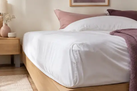 Drap-housse blanc en coton posé sur un matelas, avec un gros plan sur le bonnet et les plis du tissu.