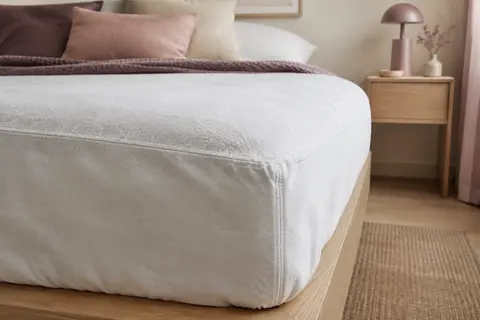 Protège-matelas en molleton de coton ajusté sur un matelas, avec un gros plan sur ses plis et ses coutures.