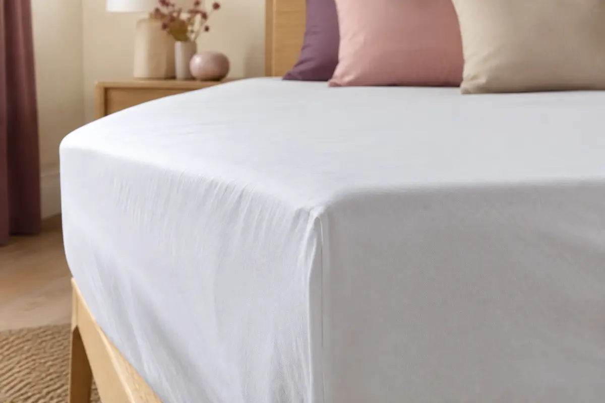 Protège-matelas blanc en forme drap-housse ajusté sur un matelas, avec un cadrage rapproché sur le tissu.