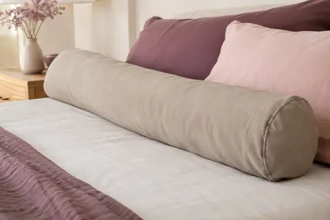 Taie de traversin en coton uni coloris Dune, posée sur un lit dans une chambre aux tons doux