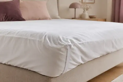 Protège-matelas blanc en coton posé sur un matelas, avec ses coins élastiques et son tissu légèrement plissé.