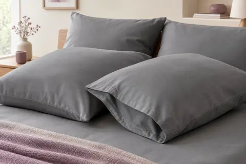 Quatre taies d’oreiller grises en microfibre brossée, posées sur un lit aux tons doux.