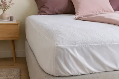 Protège-matelas blanc en éponge installé sur un lit, avec le tissu et une couture visibles de près