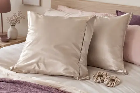 Deux taies d’oreiller carrées en satin beige clair accompagnées de deux chouchous en satin.