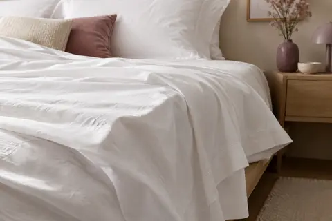 Drap plat blanc en coton disposé sur un lit, avec un tombé souple dans une chambre aux tons doux.